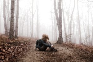 Eine Frau hockt alleine auf einem Waldweg. Es ist sehr neblig.